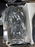 Black Nike golf shoes in a worn condition inside a damaged box, covered with plastic bag
