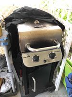Front view of the Char-Broil Performance propane grill covered with a black protective cover, showing control knobs and lower door.