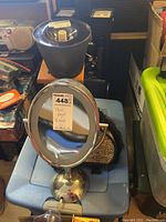 Standing hair dryer and round vanity mirror on a surface with other salon items in background.