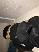 Close-up of hats hanging on the wooden hat rack, showing variety in colors and materials including black fur hat, black baseball cap and beige woven hat.