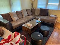 Full view of L-shaped sectional sofa in living room with microfiber cushions in various brown shades and multiple pillows. Small table and ottomans visible.