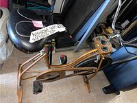 Side view of the Schwinn stationary bike showing the cushioned black seat, metallic golden bronze frame, pedals with toe clips, and part of the control console.