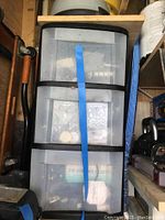 Five-drawer plastic storage bins secured with blue tape containing miscellaneous small parts and tools viewed from front.