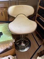 Adjustable white vinyl upholstered chair with chrome base and footrest among boxes and textiles.