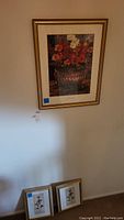 Wall display of three framed floral pictures with two smaller floral prints below a larger Renoir floral print.