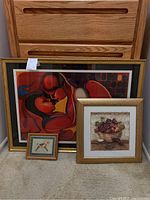 Four framed artworks grouped together including an abstract red-toned couple print, a still life of grapes, and a small bird illustration.