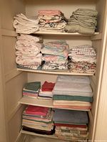 Folded bath towels and bed sheets neatly stacked on shelves in a linen closet