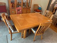 Top view of rectangular wooden dining table with parquet style wood pattern and surrounding six cushioned chairs.