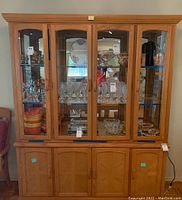 Front view of china hutch showing glass doors with display shelves holding glassware and plates, lower cabinetry with wood panel doors.