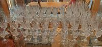 Wide view showing multiple rows of clear faceted Crystal D'Arques stemware arranged on a mirrored surface.