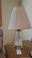 Full view of crystal base table lamp with pleated lampshade on wooden table.