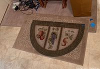 Overall shot showing three rugs stacked: large beige patterned rug, semicircular fruit design doormat, and smaller tan rectangular rug.
