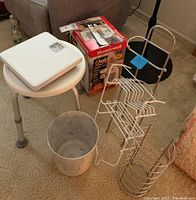 Photo shows multiple lot items including bathroom scale on stool, metal wastebasket, metal organizer racks, and boxed Honeywell heater.