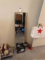 Full-length mirror standing against wall with visible dimensions approximately 12x48 inches in light-colored frame with items nearby.