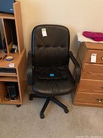 Front-facing image of the black leatherette swivel office chair showing the padded seat and backrest with armrests and five-star wheeled base.
