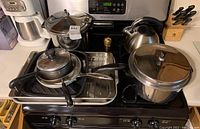 Overview of pressure cooker, bakeware pans, stovetop kettle on stove and countertop, including small gold container