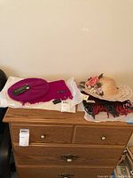 Lot items placed on wooden furniture showing a bright pink beret, decorative sun hat with floral detail, and multiple scarves.