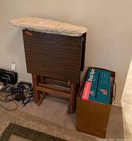 Snack/TV tables folded and standing, small ironing board on top, Family Practice Foot Spa box on floor.
