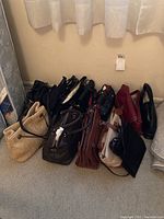 Overview photo showing assortment of 10 handbags and purses in various colors and styles arranged on floor with tag visible on wall.