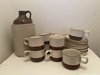 Wide shot of Denby mugs stacked and laid out in front of the vintage crock jug.