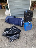 Lot overview showing sleeping bag, suitcase, BBQ cover, blue heater, and charger covered in cable