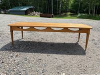 Photo of the full length side profile of the mid century coffee table outdoors on gravel showing tapered legs and decorative apron with semi-circular cutouts.