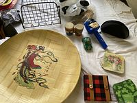 Overview of several household and decorative items arranged on a bed including bamboo tray, metal racks, ankle weights, small ceramic trays, dog figurine, jars, wind chime.