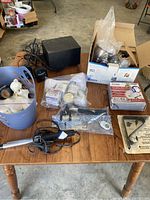 Wide view on wood table showing multiple items grouped including speakers, faucet parts, rods, selfie stick, and fireplace cover.