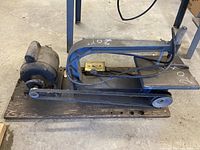 Electric scroll saw mounted on wooden base showing motor, belt, saw arm, and work surface.