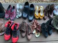 Top down view of a variety of shoes including boots, sneakers, sandals and heels laid out on wooden surface.