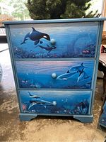 Front view of painted wooden dresser showing dolphin and marine life scenes on drawer fronts.