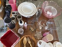 Top-down view of kitchen table with various glass bowls, wooden utensils, containers, mugs, and kitchen tools arranged neatly.