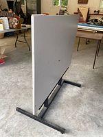 Side view of drafting table showing gray top and black metal base.