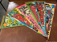 Photo of 6 colorful vintage state pennants featuring Georgia, Indiana, Hawaii, Kentucky, San Francisco, and Michigan, laid out on a brown surface.