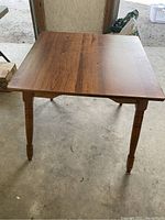 Photo showing a vintage wooden square table with turned legs and a brown finish on the tabletop.