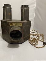 View of antique Mirroscope opaque projector showing two chimneys, rectangular metal body with circular lens opening, and fabric-wrapped cord.