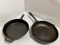 Two cast iron skillets shown side by side on white background. The Paula Deen skillet is on the right with wave pattern bottom, Lodge skillet on the left with smooth bottom.