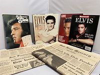 Four Elvis Presley books displayed upright with two newspapers laid below, showing the collection and visible titles and front covers