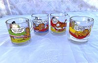 Four clear glass mugs with colorful Garfield comic prints, arranged in a row, showing various Garfield quotes and expressions.