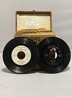 Two 45 RPM vinyl records displayed in front of the box showing label details: 'All Time Hits' by Dick Clark Presents and a black RCA Victor record.