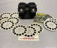 View showing the black View-Master viewer alongside eight View-Master reels spread around it, including three reels loose of Queen Elizabeth II coronation and six other reels including Yellowstone packet and various US locations.
