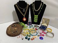 Overview of assorted vintage and retro jewelry displayed with small vintage Asian basket, showing clock belt necklace, 14k gold bracelet, peace symbol pendant, various bangles, bracelets, rings, and earrings.