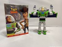 Front view of Toy Story Collector's Edition 3-disc DVD box set with Woody and Buzz Lightyear on cover, next to Buzz Lightyear figure with arms raised.