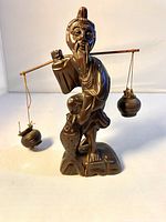 Front view of carved wooden Asian figure showing man holding fishing pole with hanging pots, on a base resembling rocks.