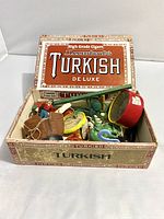 Photo of open vintage Turkish De Luxe cigar box filled with assorted small colorful vintage toys.