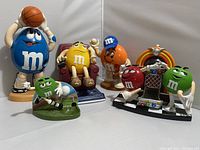 Five M&M character dispensers with thematic sport and music poses on a white backdrop. Shows full set arrangement.