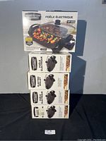 Stack of five boxed Granite Stone Diamond 12-inch electric skillets, new in box, showing front of packaging with skillet image and product details in French and English.