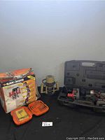 Overall lot showing Black & Decker plunge router box, Black & Decker drills inside a carrying case with charging stands, and tool bit cases.
