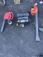 Three items on pavement: two handheld motorized blowers and one large black boat battery with attached charger.