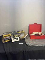 Full lot overview showing boxed car jack, jumper cables in red case, and black car mats on a table.